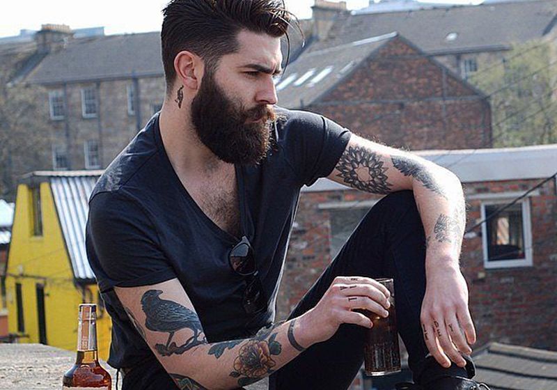 modelo masculino com barba sentado em paisagem industrial