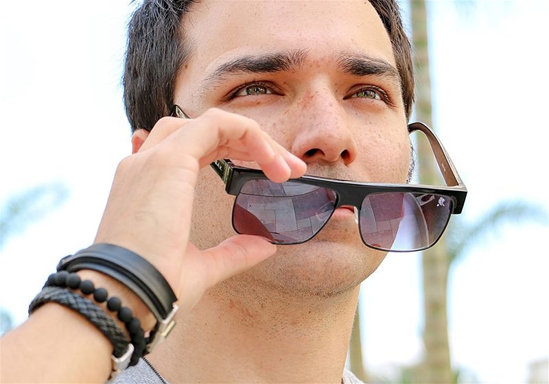 Imagem aproximada do rosto de um modelo masculino usando óculos escuros e acessórios no braço