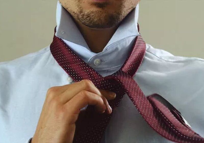 Homem colocando a ponta mais ampla da gravata por baixo da menor
