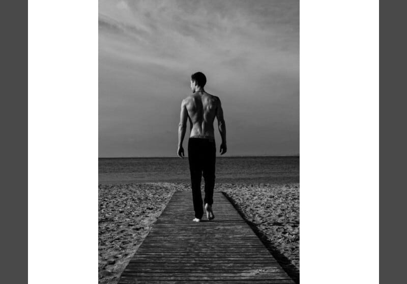 homem de calça e sem camisa caminhando na praia 