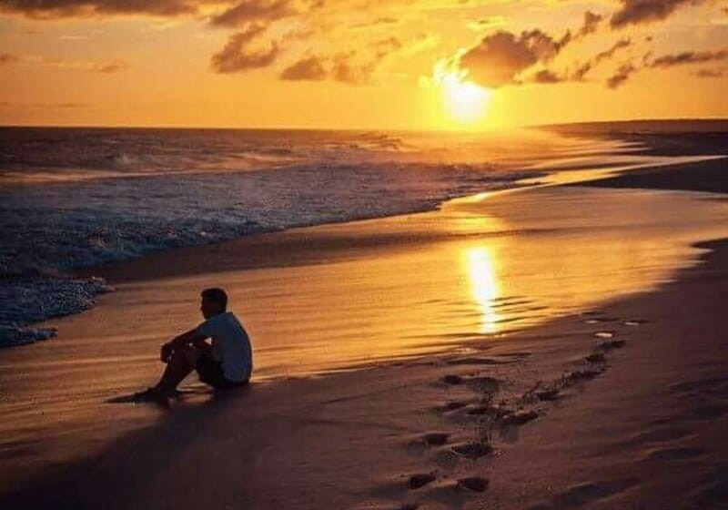 homem sentado na praia com o pôr do sol ao fundo
