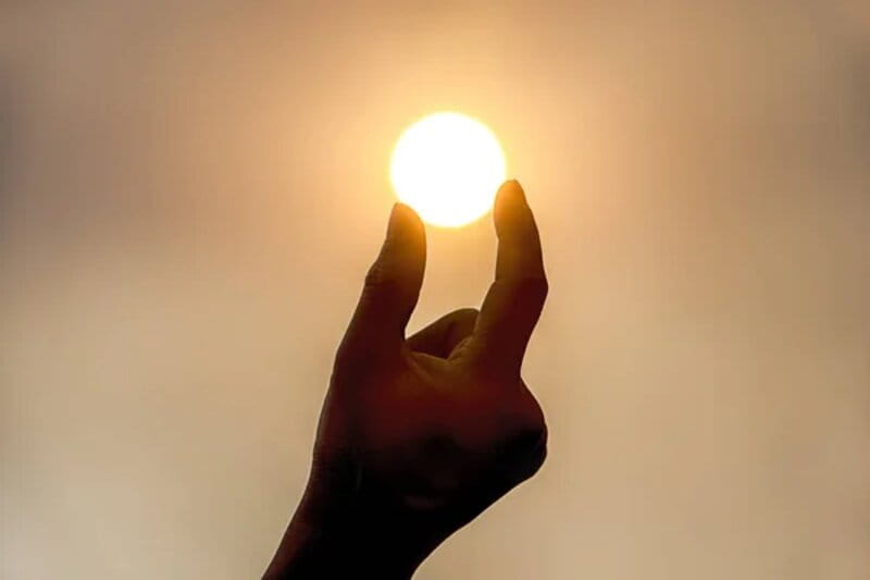 perspectiva da pessoa segurando o sol com os dedos