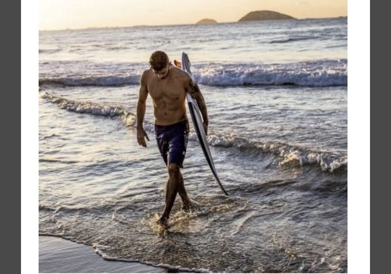 homem saindo do mar com uma prancha de surf