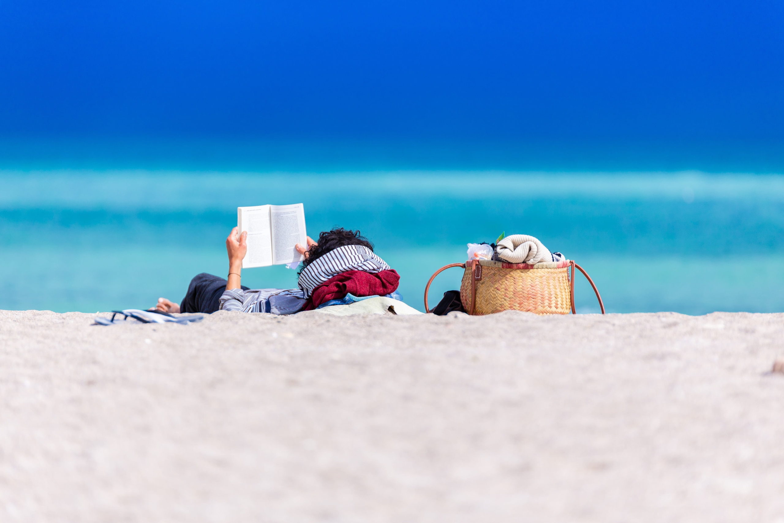 pessoa deitada na praia lendo um livro
