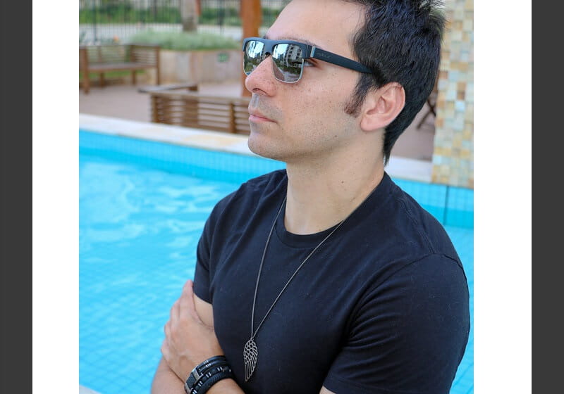 modelo próximo à piscina utilizando uma camiseta preta e um óculos de sol
